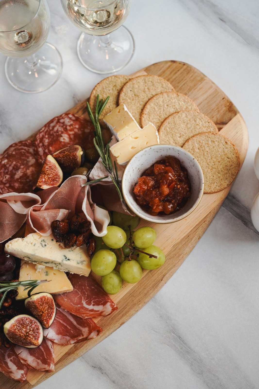 A board of charcuterie, cheese, figs and grapes next to glasses of white wine