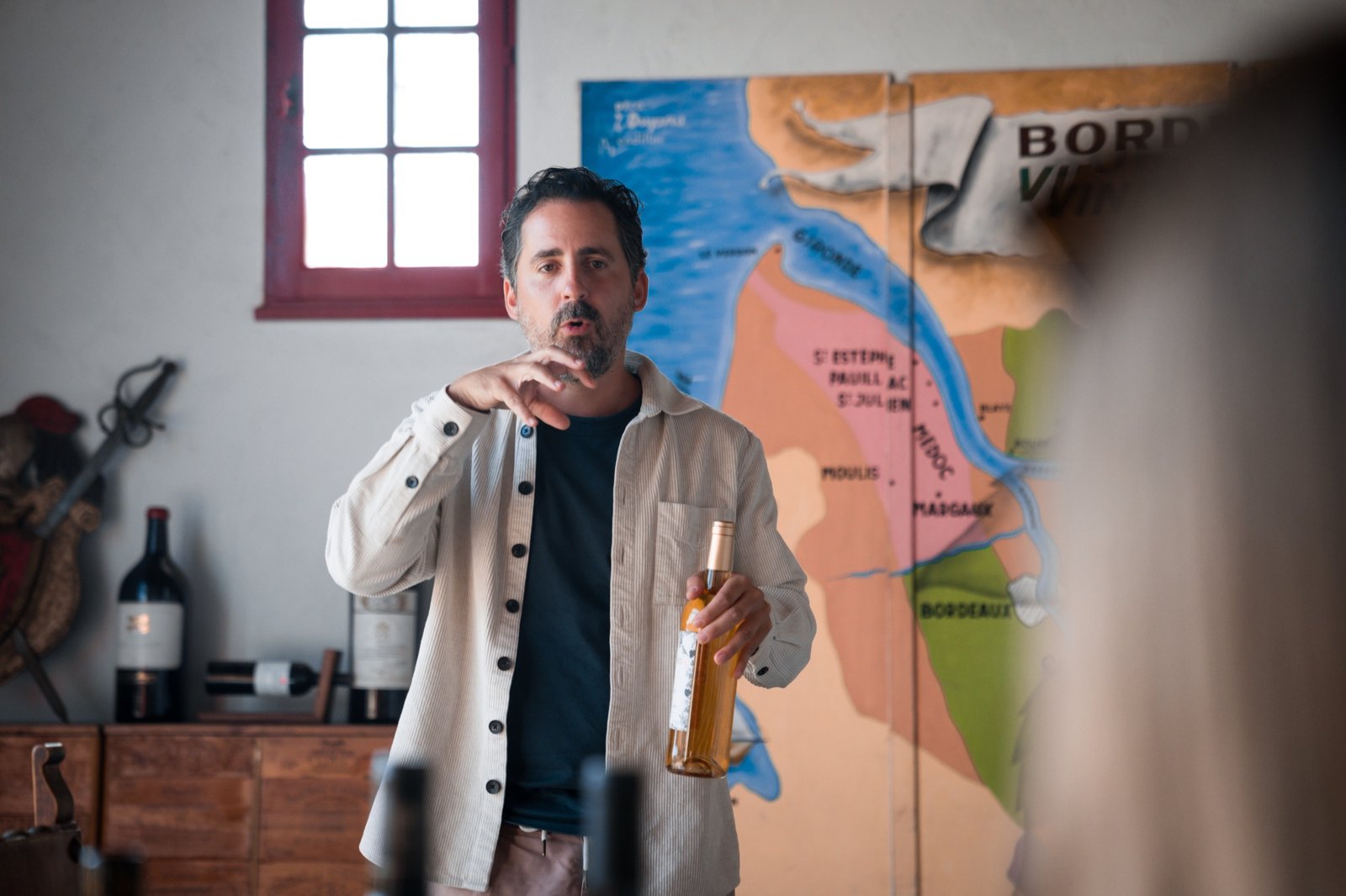 Gildas presenting a bottle during a tasting, a map of Bordeaux behind him