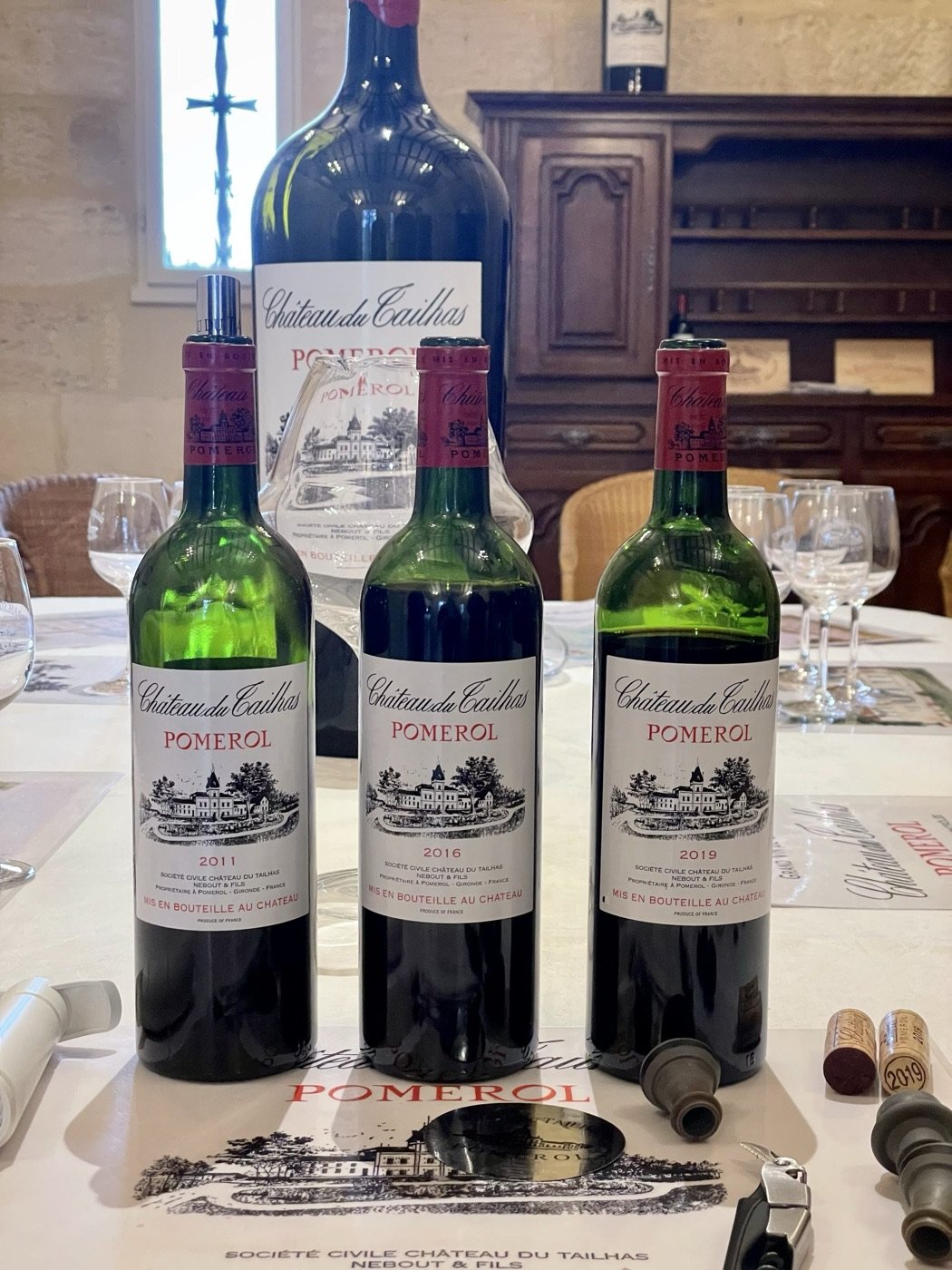 Three bottles of Bordeaux on a tasting table with corks and a notebook